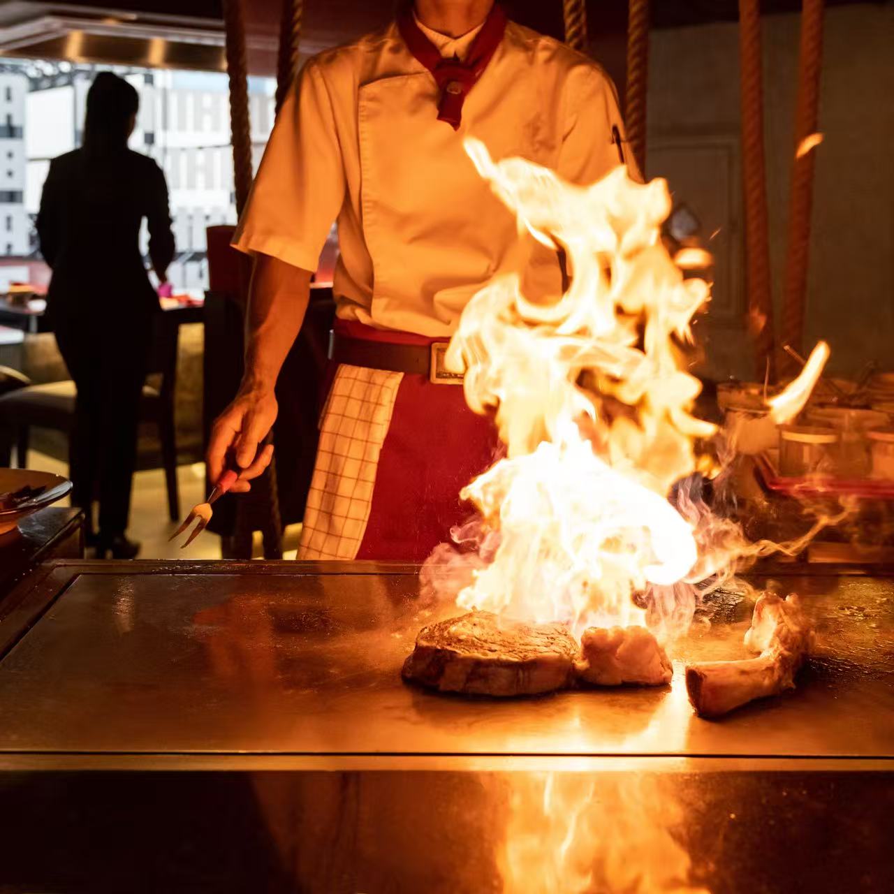 EZ Hibachi chef flaming a premium cut of steak at the teppanyaki grill — tableside action shot